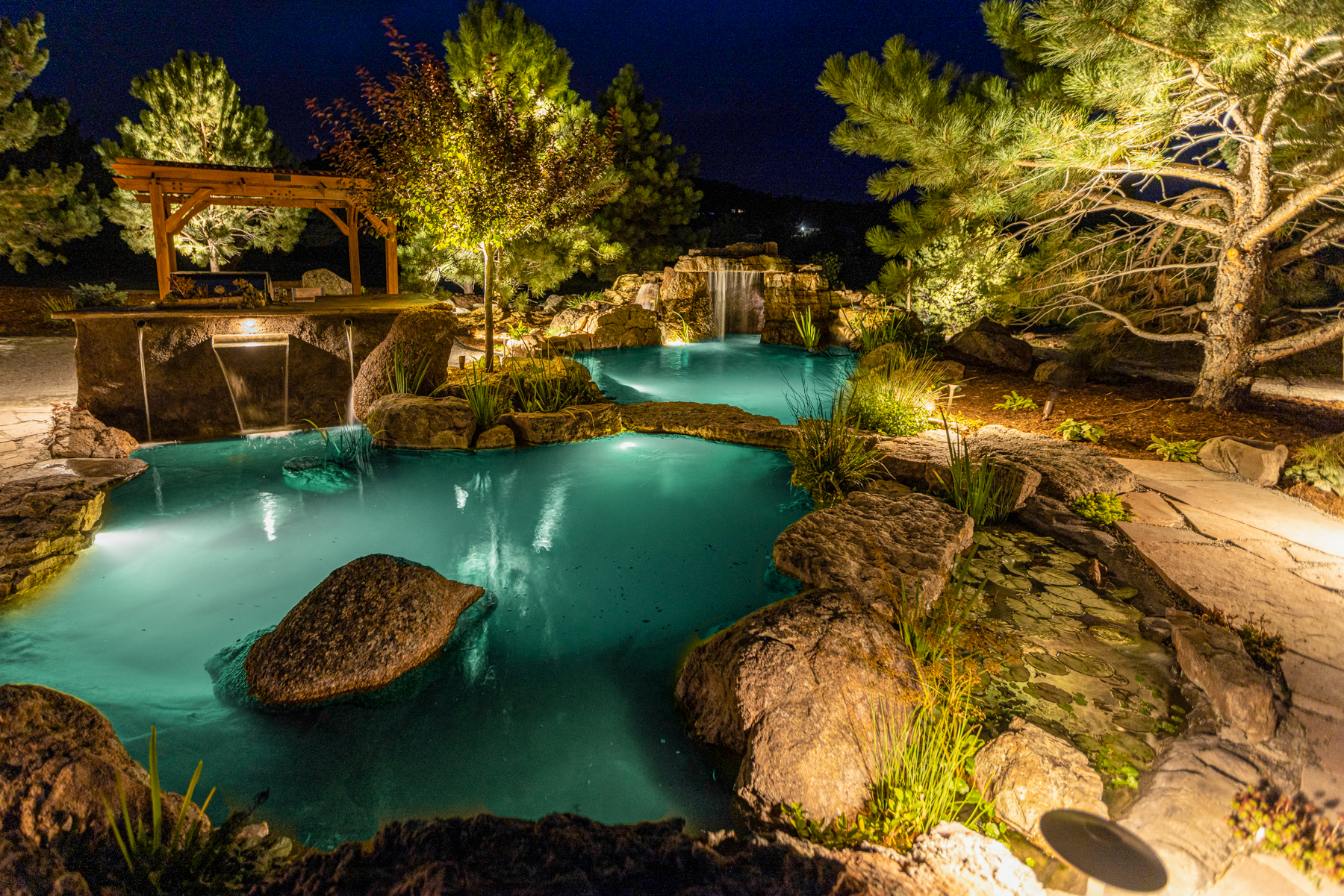 photo of a large natural rock water feature at night with underwater lighting and aquatic plants